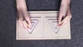 Female hands holding colored pencils and drawing lines in symmetrical double-sided triangular maze stencil made of wood