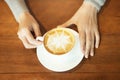 Female hands holding cup of coffee with cobweb shape foam over ready to drink on rustic wooden table Royalty Free Stock Photo