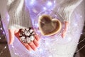 Female hands holding cup of coffee and cookies in Christmas lights. Heart shape. Top view Royalty Free Stock Photo