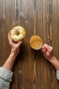 Female hands holding cup of coffee and donut in a white glaze with yellow confectionery sprinkles on a wooden background Royalty Free Stock Photo