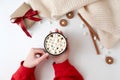 Female hands holding cup of hot chocolate with marshmallow. Christmas beverage, tasty cookies, gift box on white background. Royalty Free Stock Photo