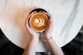 Female hands holding a cup of hot coffee with foam over a wooden table. View from above. Great morning. Royalty Free Stock Photo