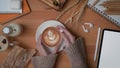 Female hands holding a cup of latte coffee on wooden worktable with mock up tablet and supplies Royalty Free Stock Photo