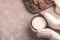 Female hands are holding cup of warm milk, chocolate cookies on