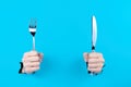 Hands are holding cutlery metal knife and fork in torn hole Royalty Free Stock Photo