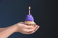 Female hands holding delicious birthday cupcake with burning candle on dark background Royalty Free Stock Photo