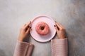 Female hands holding donut on pink plate over stone background. Top view, flat lay. Sweet, dessert, diet concept. Weight lost