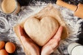 Female hands holding dough in heart shape top view. Baking ingredients on the dark wooden table Royalty Free Stock Photo