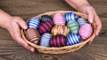 Female hands holding Easter eggs in wicker basket on wooden table detail