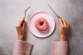 Female hands holding fork and knife cutting donut on pink plate over stone background. Top view, flat lay. Sweet, diet concept. Royalty Free Stock Photo