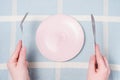 Female hands holding a fork and and knife next to an empty pink plate on a blue tablecloth background close-up top view. Royalty Free Stock Photo