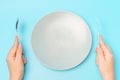 Female hands holding a fork and spoon next to an empty plate on a blue background close-up top view Royalty Free Stock Photo