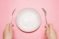Female hands holding a fork and spoon next to an empty plate on a pink background close-up top view. Royalty Free Stock Photo