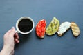 Female Hands Holding A Fresh Cup Of Coffee In Black Background Top View . Fresh sandwiches with soft cheese, strawberries and kiwi