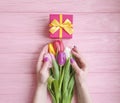 Female hands holding a gift box birthday , romantic a bouquet of tulips on a wooden background Royalty Free Stock Photo