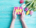 Female hands holding a gift box, holiday spring celebration romance a bouquet of tulips on a blue wooden background Royalty Free Stock Photo