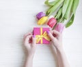 Female hands holding a gift box spring anniversary birthday , romantic a bouquet of tulips on a wooden background Royalty Free Stock Photo
