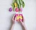 Female hands holding a gift box anniversary holiday birthday , romantic a bouquet of tulips on a wooden background Royalty Free Stock Photo
