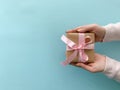 Female hands holding gift box with pastel pink ribbon on soft blue color background Royalty Free Stock Photo