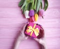 Female hands holding a gift box present birthday , romantic a bouquet of tulips on a wooden background Royalty Free Stock Photo