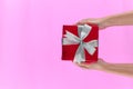 Female hands holding gift box wrapped in red paper with ribbon on pink colour background. Top view. Copy space for text. Holiday Royalty Free Stock Photo