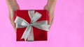 Female hands holding gift box wrapped in red paper with ribbon on pink colour background. Top view. Copy space for text. Holiday Royalty Free Stock Photo