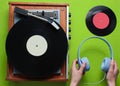 Female hands holding headphones against the background of retro vinyl record player with vinyl records on green background. Royalty Free Stock Photo