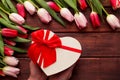 Female hands holding a heart-shaped gift box on a dark wooden background with beautiful tulips flowers.Festive greeting card for Royalty Free Stock Photo