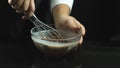 Female hands holding an iron whisk for stirring liquid chocolate cream, pastry, isolated black background Royalty Free Stock Photo