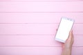 Female hands holding mobile phone with blank screen on pink wood background. Smartphone on wood table Royalty Free Stock Photo