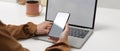 Female hands holding mock up smartphone while sitting at worktable with mock up laptop in home office Royalty Free Stock Photo