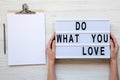 Female hands holding modern board with text `Do what you love`. Blank noticepad with pencil. White wooden background, top view. Royalty Free Stock Photo