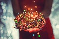 Female hands holding Multicolored Christmas light decorations on dark holiday background. Xmas and New Year theme. Toning Royalty Free Stock Photo