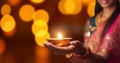 Female hands holding oil lamp celebrating Diwali, beautiful lights bokeh background. Generative AI