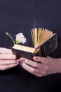 Female hands holding open vintage prayer book and pink carnation flower on a black background Royalty Free Stock Photo