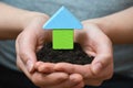 Female hands holding a piece of land with wooden house. Ecological home, construction and real estate concept. Royalty Free Stock Photo