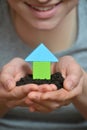 Female hands holding a piece of land with wooden house. Ecological home, construction and real estate concept. Royalty Free Stock Photo