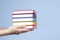 Female hands holding pile of books over light blue background. Education, self-learning, book swap, hobby, relax time