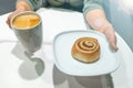 Female hands holding plate with cinnamon roll. Royalty Free Stock Photo