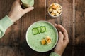 Female hands holding a plate cold soup cucumber on a wooden table, top view. Healthy vegan food.
