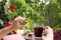 Female hands holding pomegranate, cherry juice, fruit drink in a glass mug and French pasta in the garden, flowers of climbing Royalty Free Stock Photo