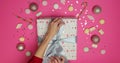 Female hands holding present box wrapped in festive paper and tied with backers twine on pink background with decor