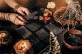 A woman& x27;s hands hold raven feathers against a backdrop of magical patterned cards and lit candles. Halloween