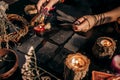 A woman& x27;s hands hold raven feathers against a backdrop of magical patterned cards and lit candles. Halloween