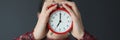 Female hands holding red alarm clock in front of face closeup