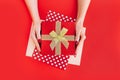 Female hands holding red goft box present with golden bow on red background. Festive backdrop for holidays: Birthday Royalty Free Stock Photo