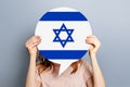 Female hands holding a round information piece of paper dialog with israel flag isolated over grey studio background