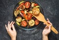 Female hands holding a shoulder blade. Roasted vegetables mix on plate on black stone background. Royalty Free Stock Photo