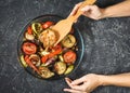Female hands holding a shoulder blade. Roasted vegetables mix on plate on black stone background Royalty Free Stock Photo