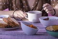 Female hands holding and stirring a cup surrounded by bread on a plate and an assortment of bowls with dry fruits on a wooden